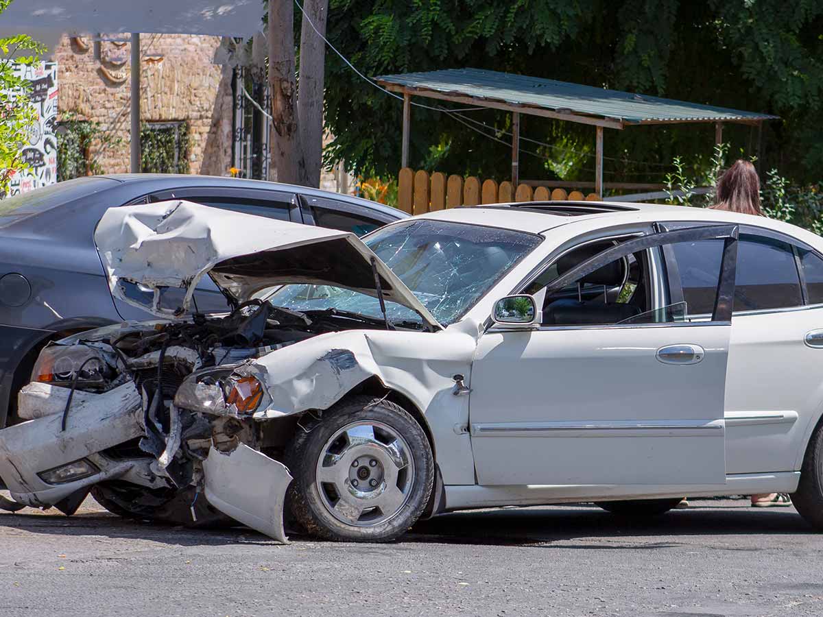 White car with crushed hood on road side.