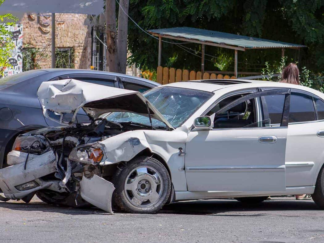A white sedan with a smashed front end and open hood sits on the street after a car accident, a scene often handled by an injury law firm.