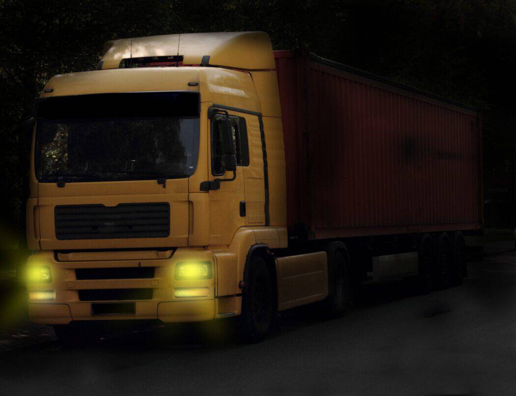 A yellow semi-truck with a red cargo container parked on a dark road, a common site for an injury lawyer.