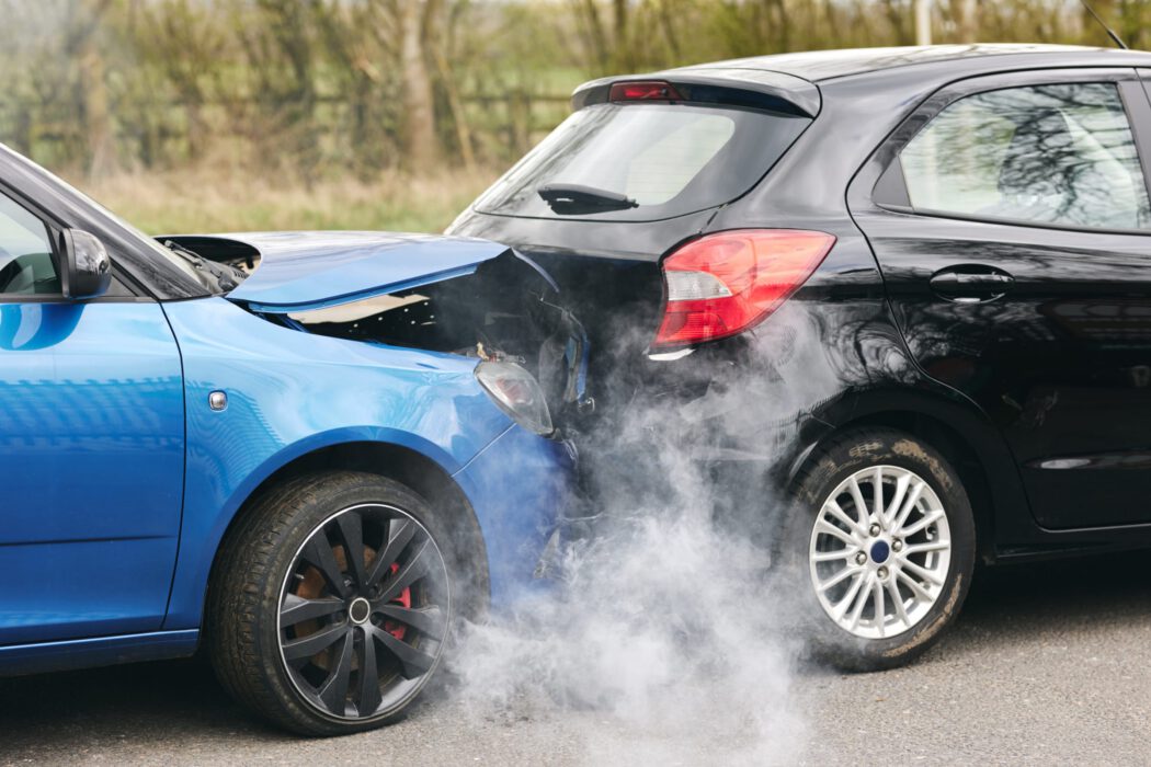 A blue car has crashed into a black car, leaving smoke rising from the damaged front end in a scene often handled by an injury law firm.