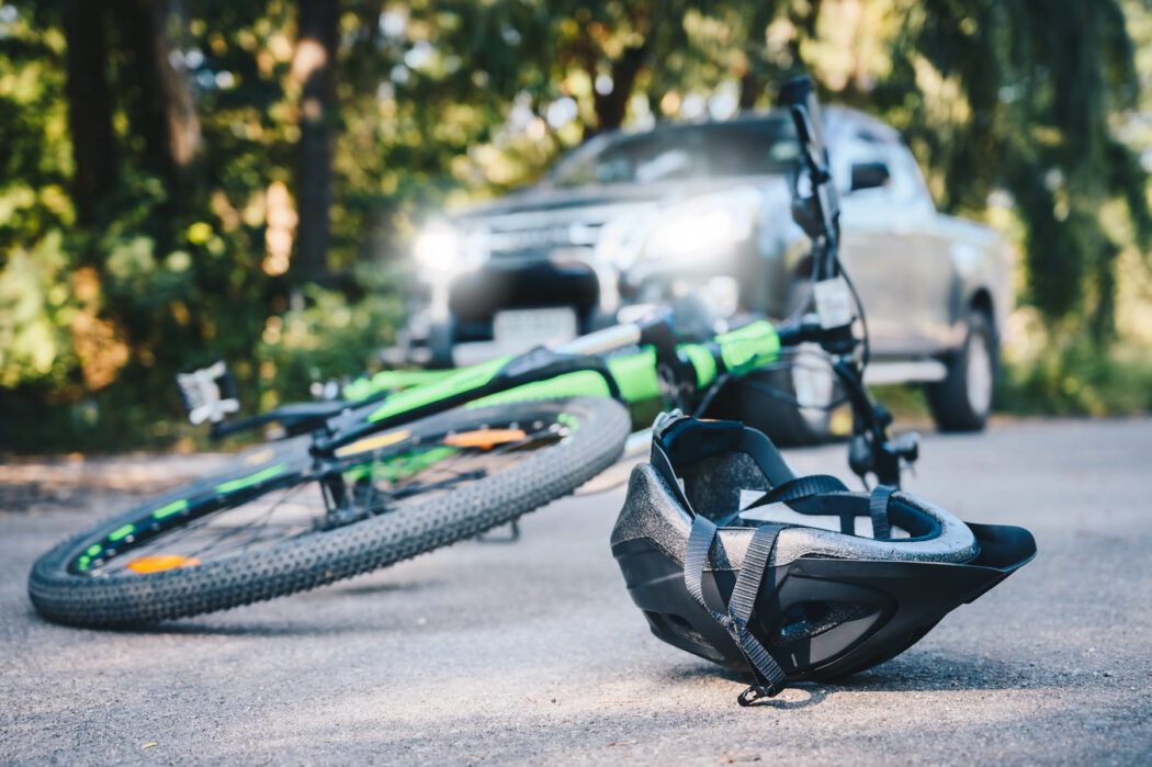 A bicycle and a helmet lying on the road in front of a car, a scene often handled by an injury lawyer.