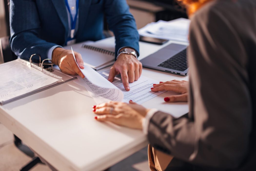 Two people in business attire sit across from each other at a desk while an injury lawyer reviews a document with a client.