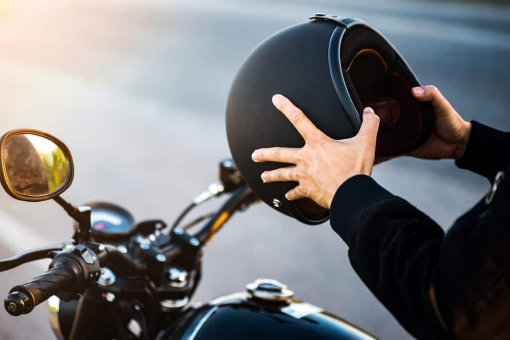 A person sits on a motorcycle holding a black helmet, a scenario often handled by an injury lawyer.