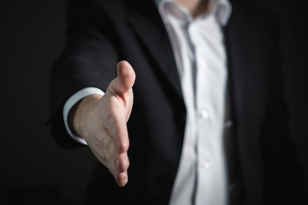 A person in a suit jacket and white shirt extending their hand for a handshake with an injury lawyer.