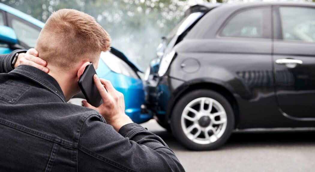 A man holds his neck while talking to an injury lawyer near two vehicles involved in a car accident.