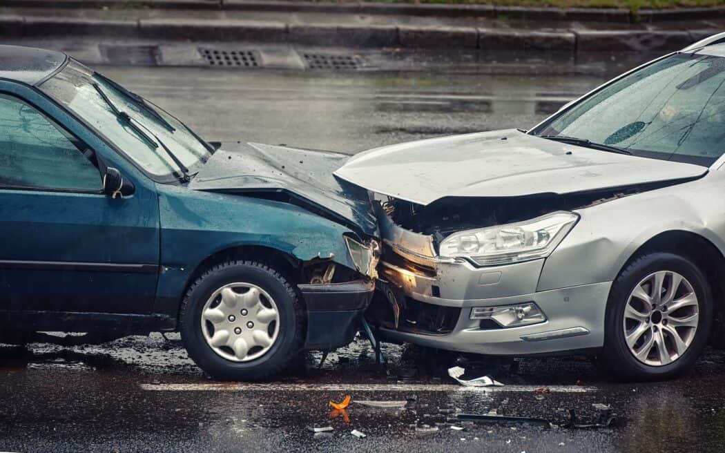 A teal car and a silver car involved in a head-on collision on a wet street.